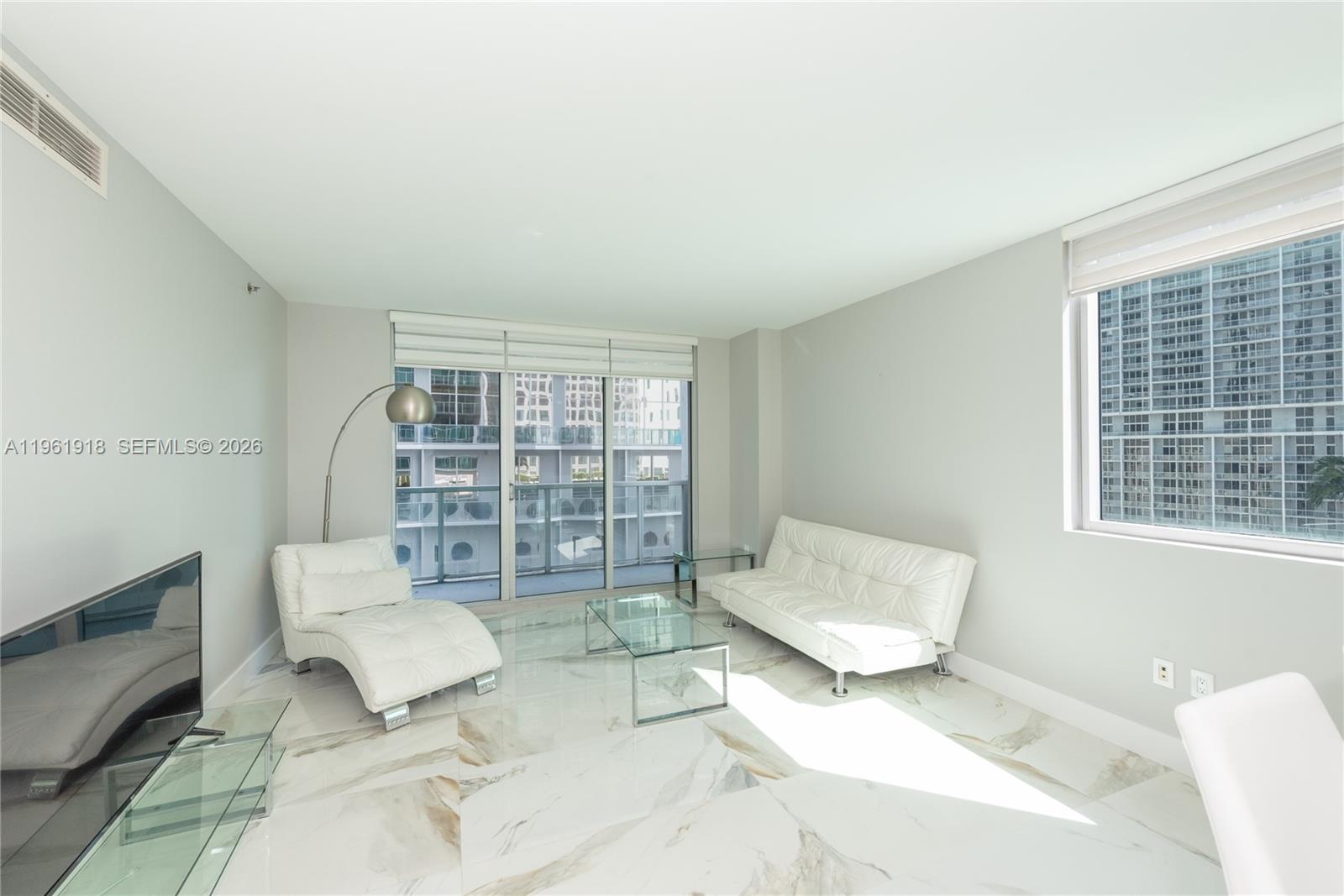A living room features white leather furniture, a glass coffee table, and marble-patterned tile flooring — 55 SE 6 ST # 1207, Miami FL 33131, MIAMI, FL