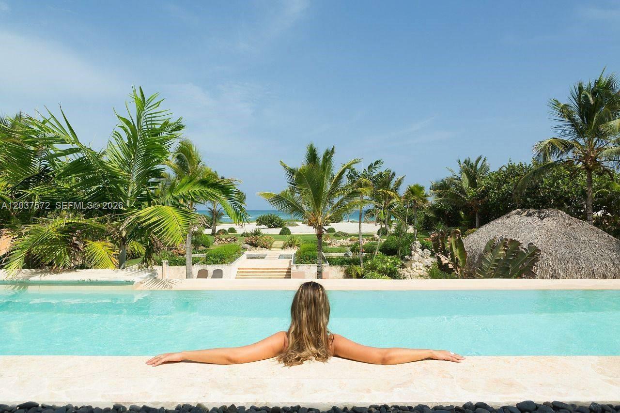 A woman looks out from an infinity pool toward a tropical garden and the ocean — 0 Cana cap, FL, FL