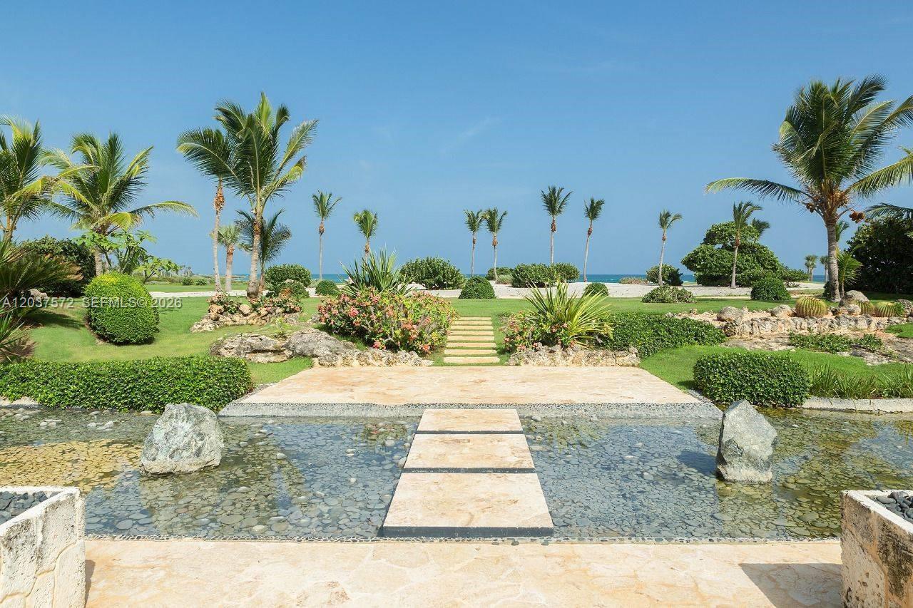 A stone walkway crosses a shallow reflecting pool toward a grassy lawn with palm trees — 0 Cana cap, FL, FL