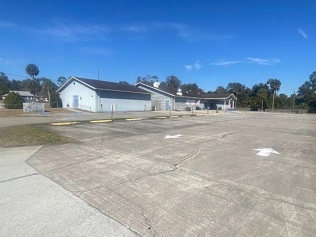 A low-rise commercial building with a large concrete parking lot under a clear blue sky — 301 W BLUE SPRINGS AVENUE, ORANGE CITY, FL
