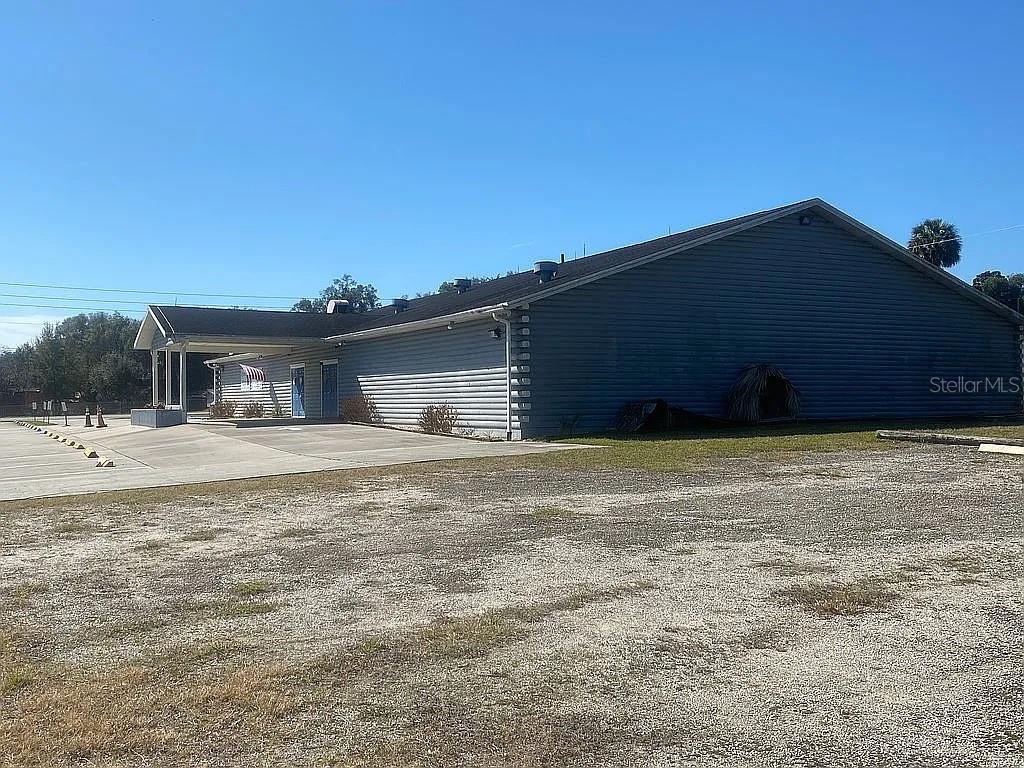 A single-story building with gray horizontal siding features a covered entrance and a gravel lot — 301 W BLUE SPRINGS AVENUE, ORANGE CITY, FL