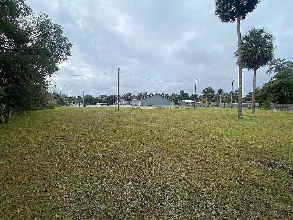 A large, grassy vacant lot with palm trees and a distant building under a cloudy sky — 301 W BLUE SPRINGS AVENUE, ORANGE CITY, FL
