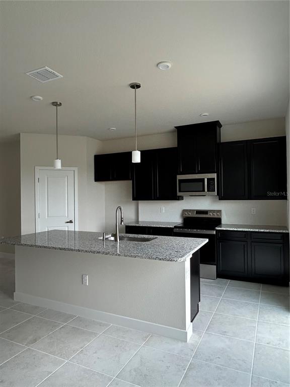 A kitchen features black cabinets, granite countertops, a center island, and light-colored tile flooring — 1838 KENDALL POINTE PLACE, MELBOURNE, FL