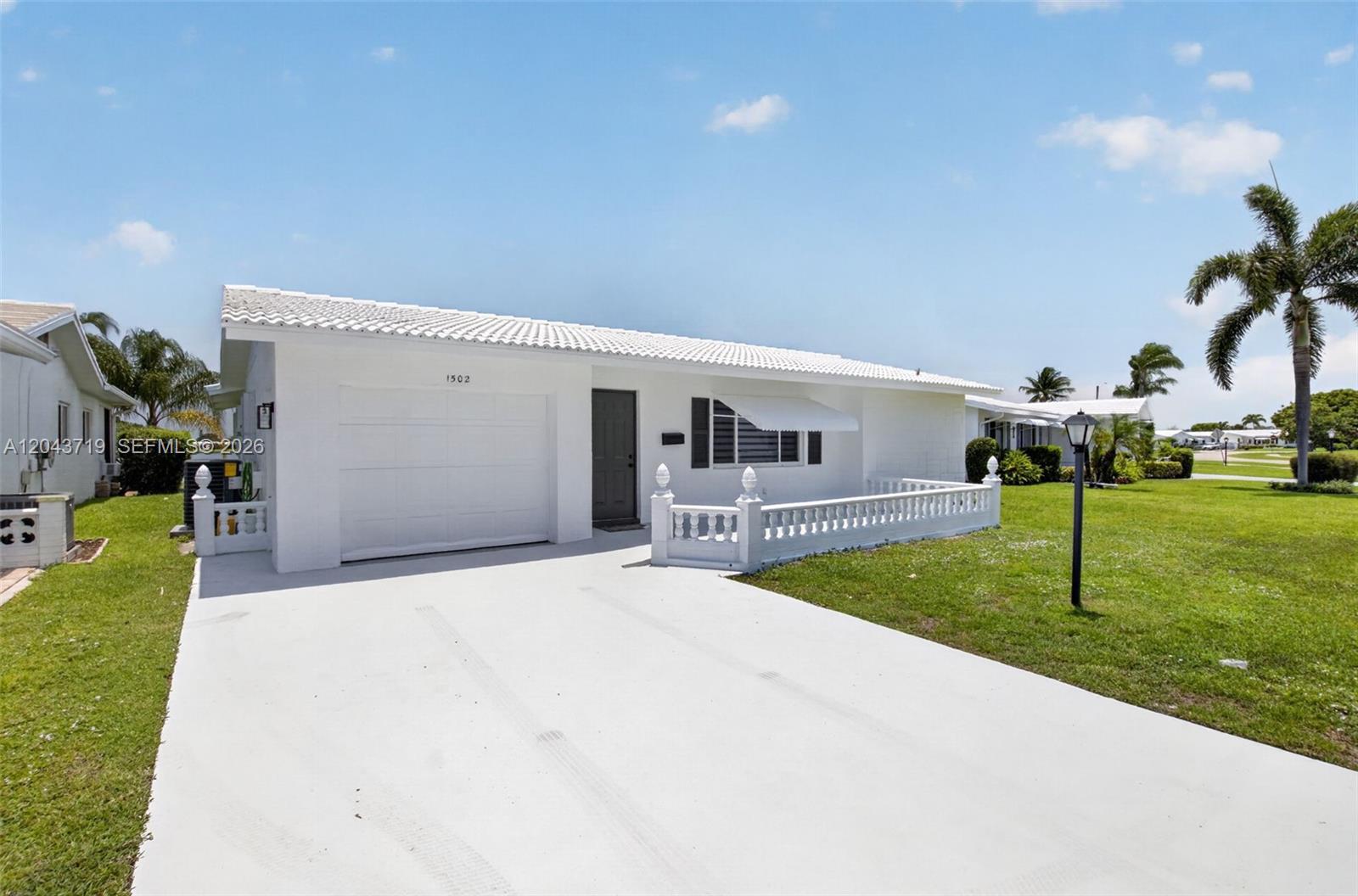 A white single-story house features a garage, a small front patio, and a palm tree — 1502 SW 17th Ave, Boynton Beach FL 33426, BOYNTON BEACH, FL