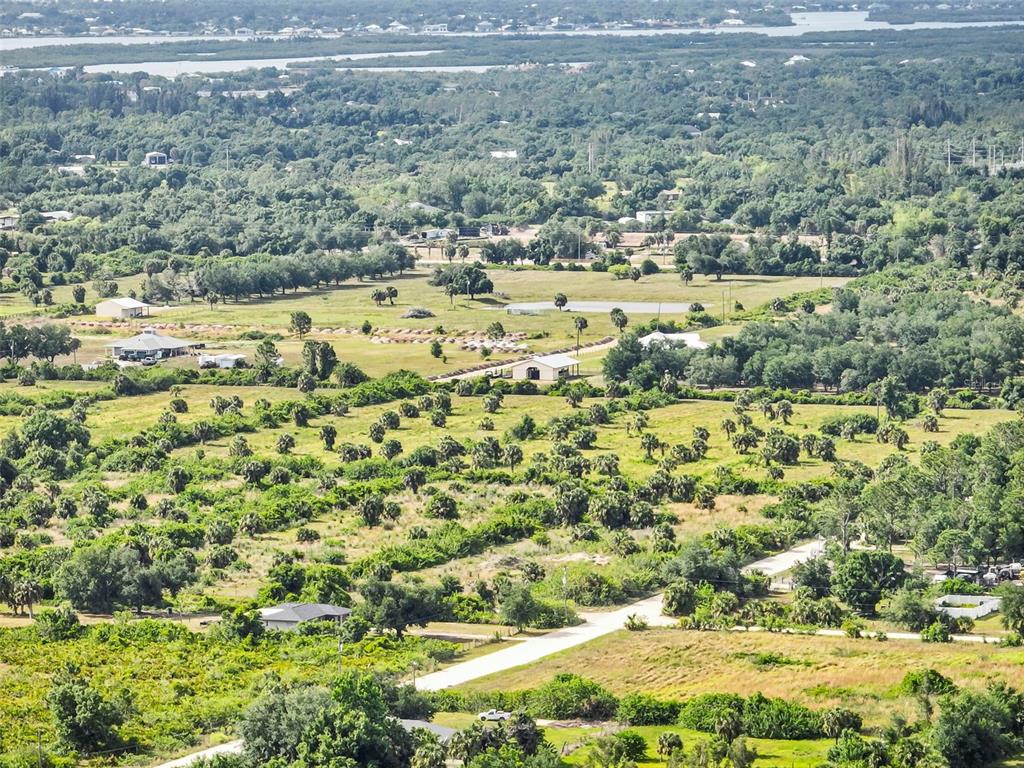 An aerial view shows a rural landscape with scattered trees, grassy fields, and several buildings — 6211 GROVE BOULEVARD, PUNTA GORDA, FL
