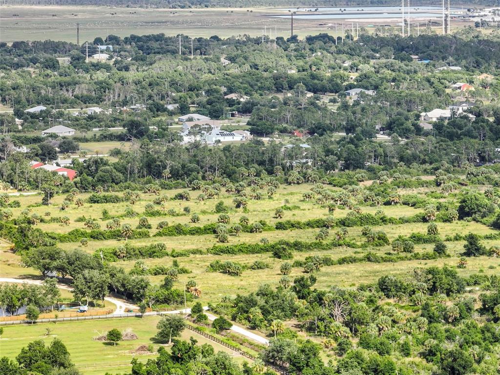 An aerial view shows a rural landscape with scattered trees, grassy fields, and distant houses — 6211 GROVE BOULEVARD, PUNTA GORDA, FL