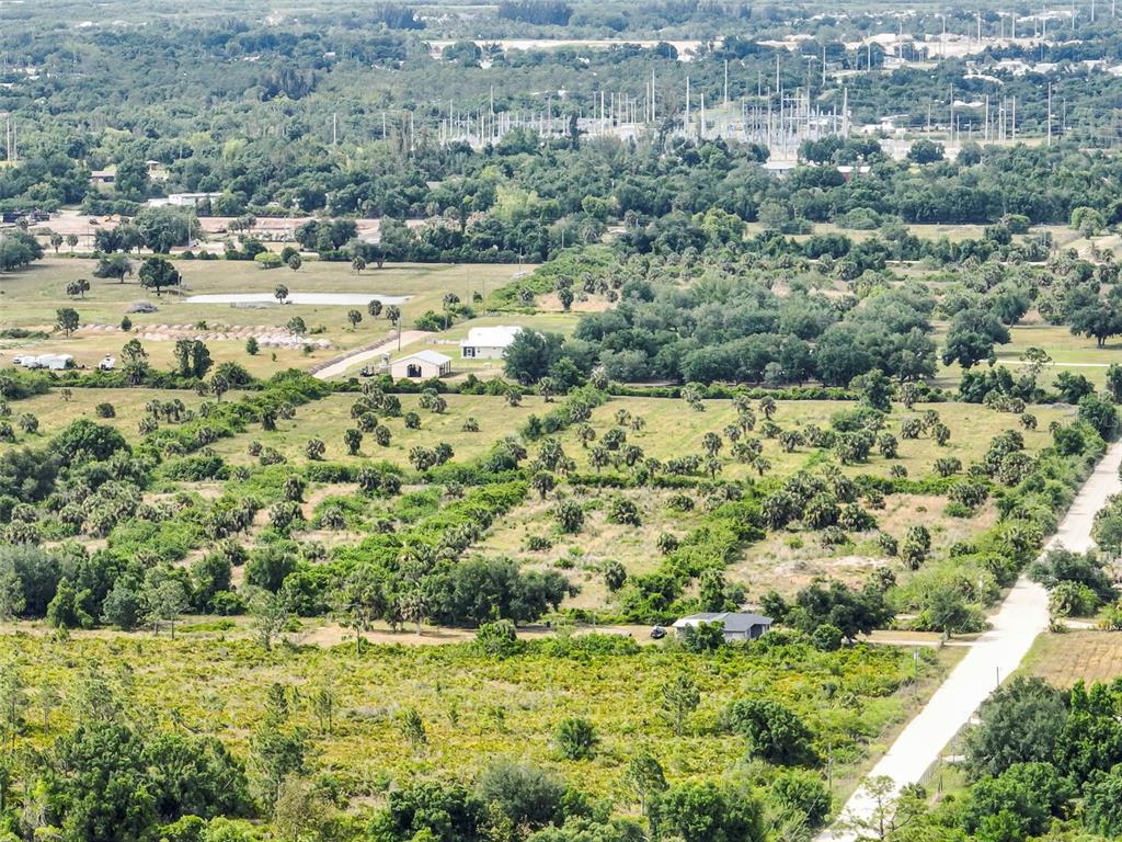 An aerial view shows a rural landscape with scattered trees, a dirt road, and several buildings — 6211 GROVE BOULEVARD, PUNTA GORDA, FL