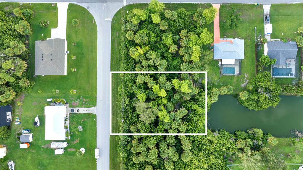 An aerial view shows a vacant, wooded lot situated between two residential properties and a canal — 5016 SILVER BELL DRIVE, PORT CHARLOTTE, FL