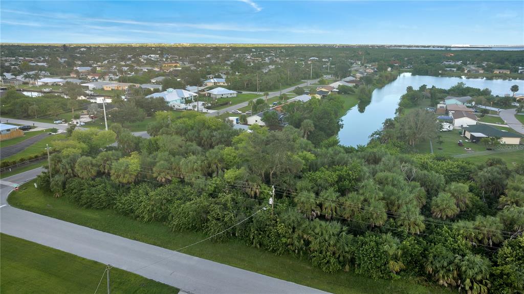 An aerial view shows a vacant, tree-covered lot situated between a residential street and a canal — 5016 SILVER BELL DRIVE, PORT CHARLOTTE, FL