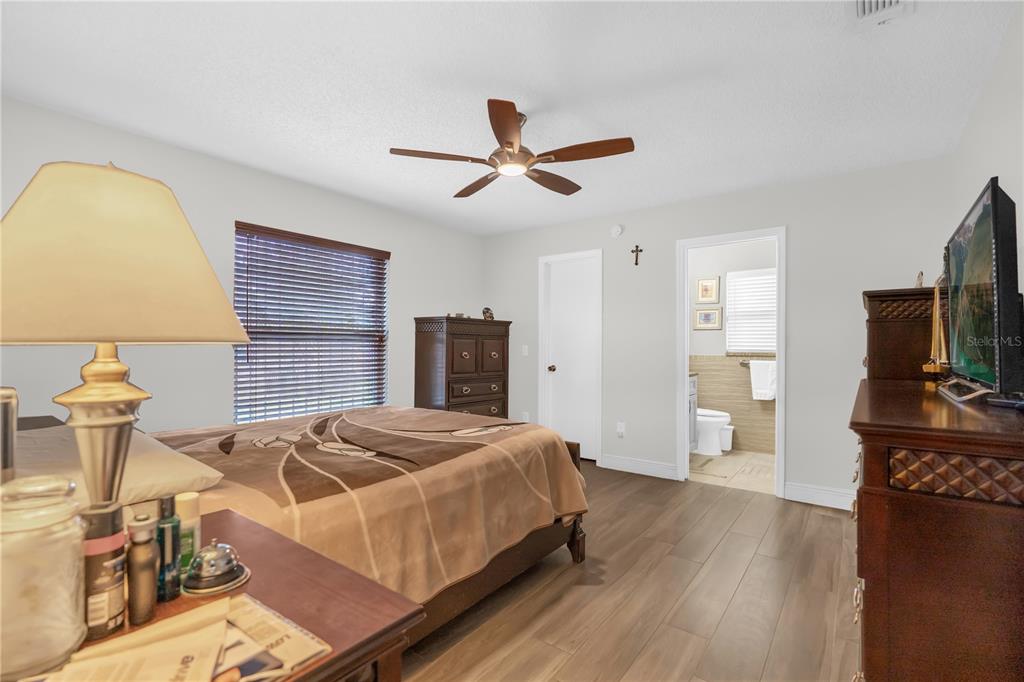 A bedroom with wood-look flooring, a ceiling fan, a bed, and an attached bathroom — 7702 LEGACY LANE, ORLANDO, FL