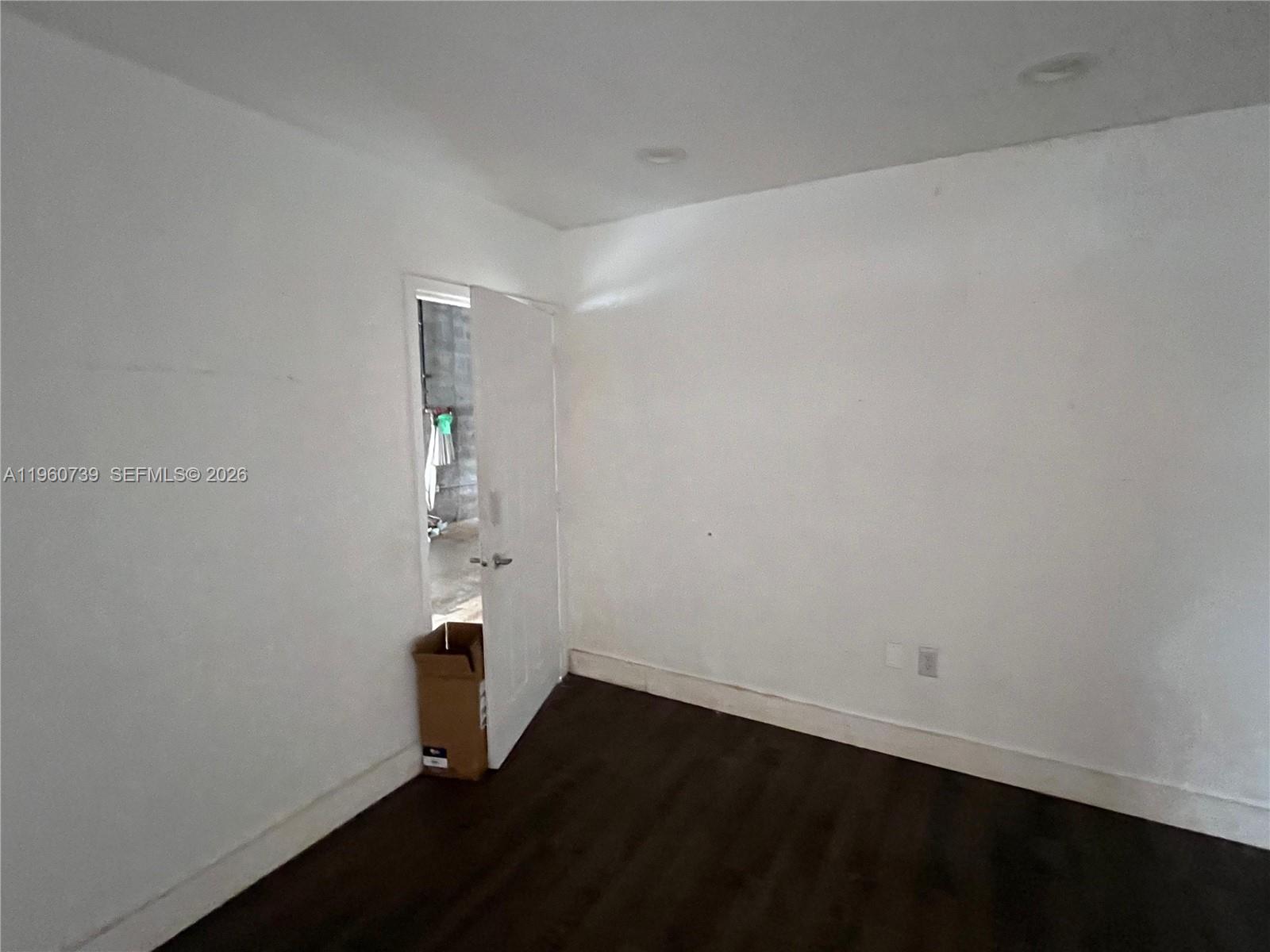 An empty room features white walls, dark wood-look flooring, and an open doorway — 12361 SW 128th Ct # 203, Miami FL 33186, MIAMI, FL