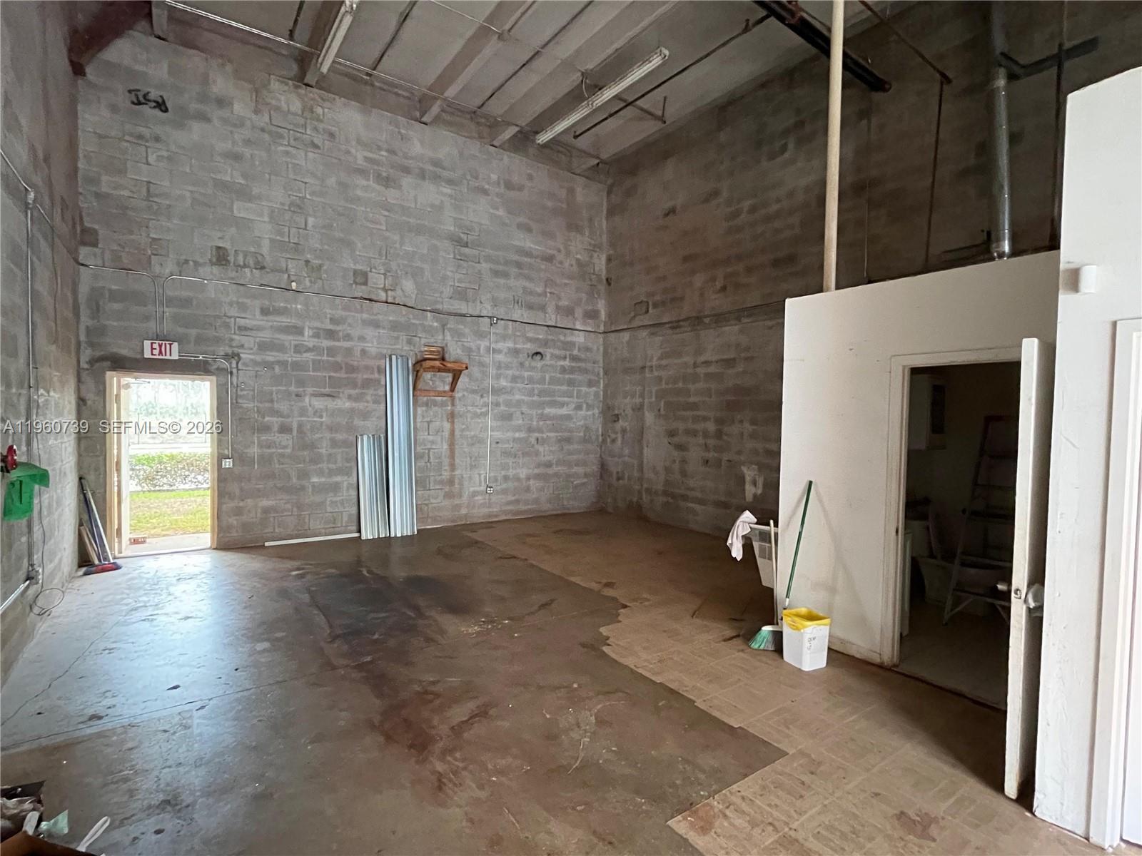 An industrial warehouse space features exposed concrete block walls, a concrete floor, and an exit door — 12361 SW 128th Ct # 203, Miami FL 33186, MIAMI, FL