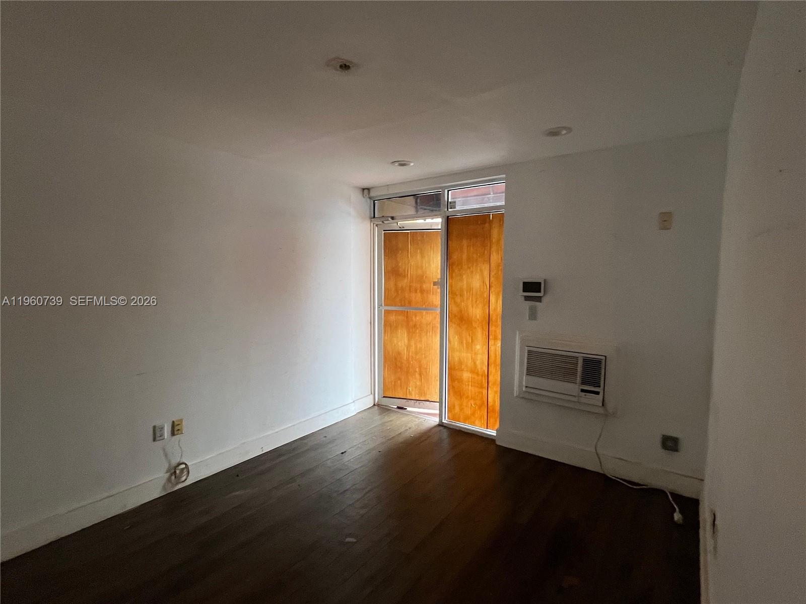 An empty room features dark wood flooring, white walls, and a glass door with wood panels — 12361 SW 128th Ct # 203, Miami FL 33186, MIAMI, FL