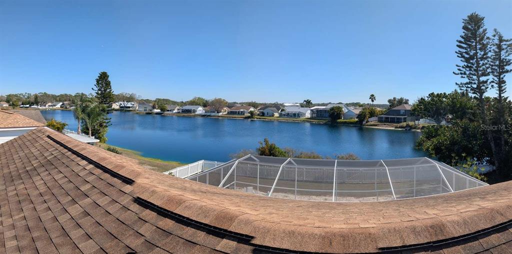An elevated view shows a shingled roof overlooking a screened pool enclosure and a lake — 4826 11TH AVENUE CIRCLE E, BRADENTON, FL