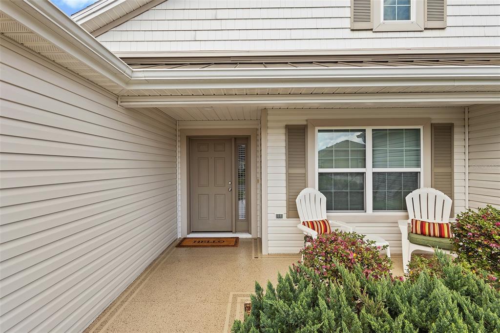 A covered front porch features light-colored siding, a tan door, and two white chairs — 3258 HOLLEY TERRACE, THE VILLAGES, FL