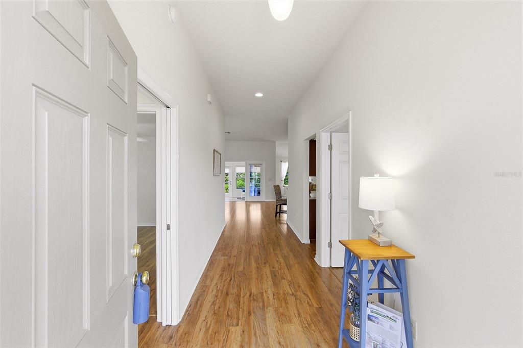 A hallway with wood-look flooring leads from an entryway toward a bright living area — 3258 HOLLEY TERRACE, THE VILLAGES, FL