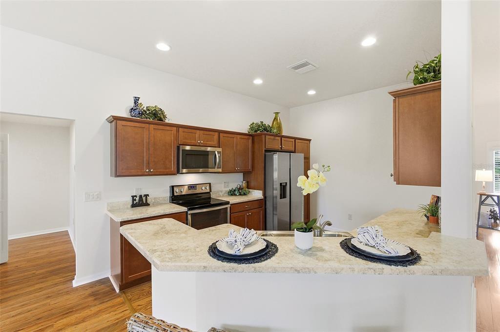 A kitchen features wood cabinets, stainless steel appliances, and a peninsula with a stone countertop — 3258 HOLLEY TERRACE, THE VILLAGES, FL