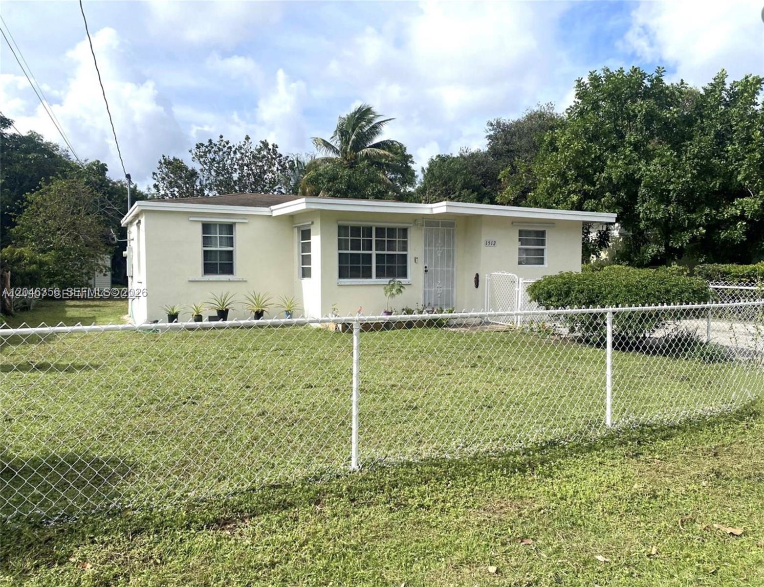 A single-story house with a light yellow exterior sits behind a white chain-link fence — 1512 N 58th Ave, Hollywood FL 33021, HOLLYWOOD, FL