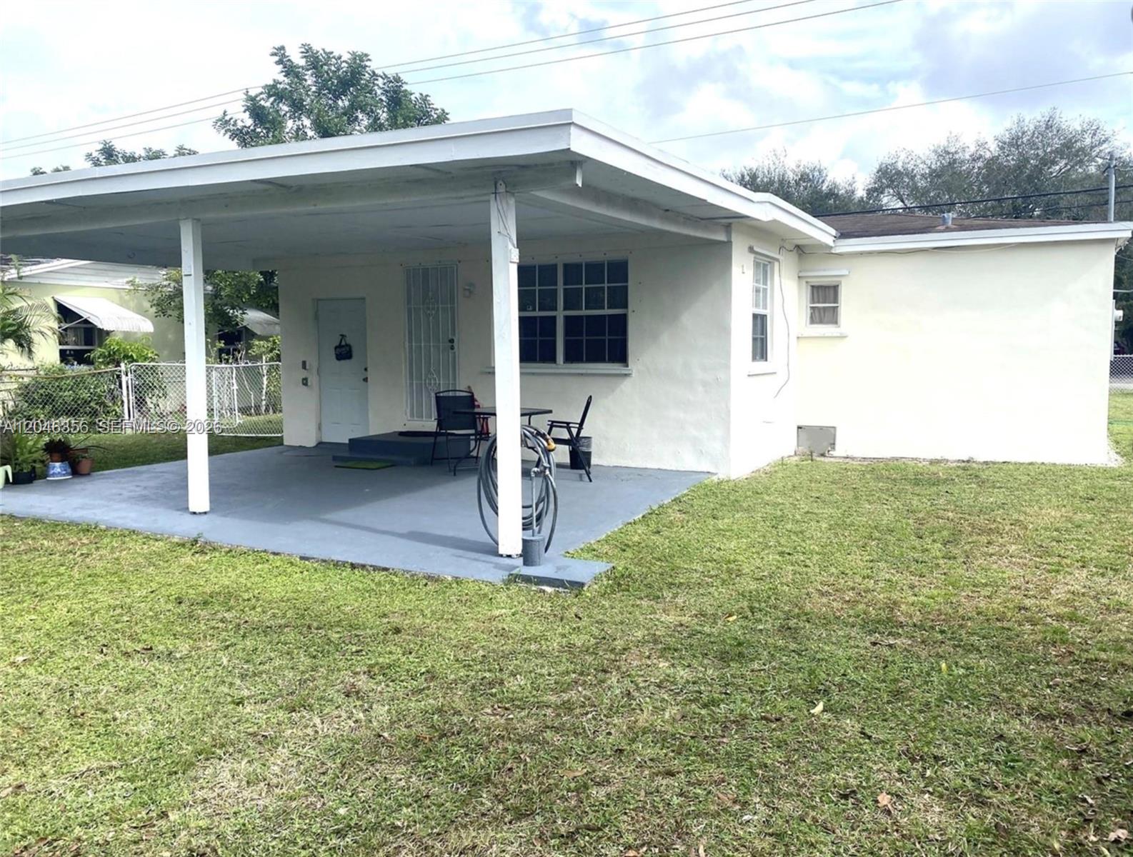 A white house features a covered concrete patio, a lawn, and a metal security door — 1512 N 58th Ave, Hollywood FL 33021, HOLLYWOOD, FL