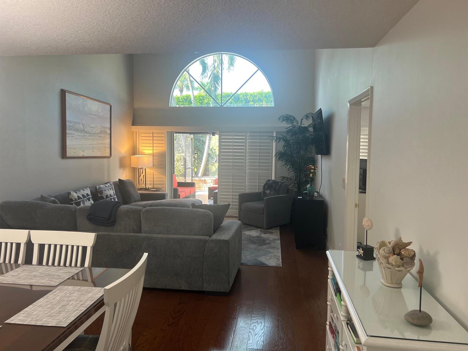 A living room with a vaulted ceiling, arched window, grey sectional sofa, and hardwood floors — 1209 Ocean Dunes Circle, Jupiter FL 33477, JUPITER, FL
