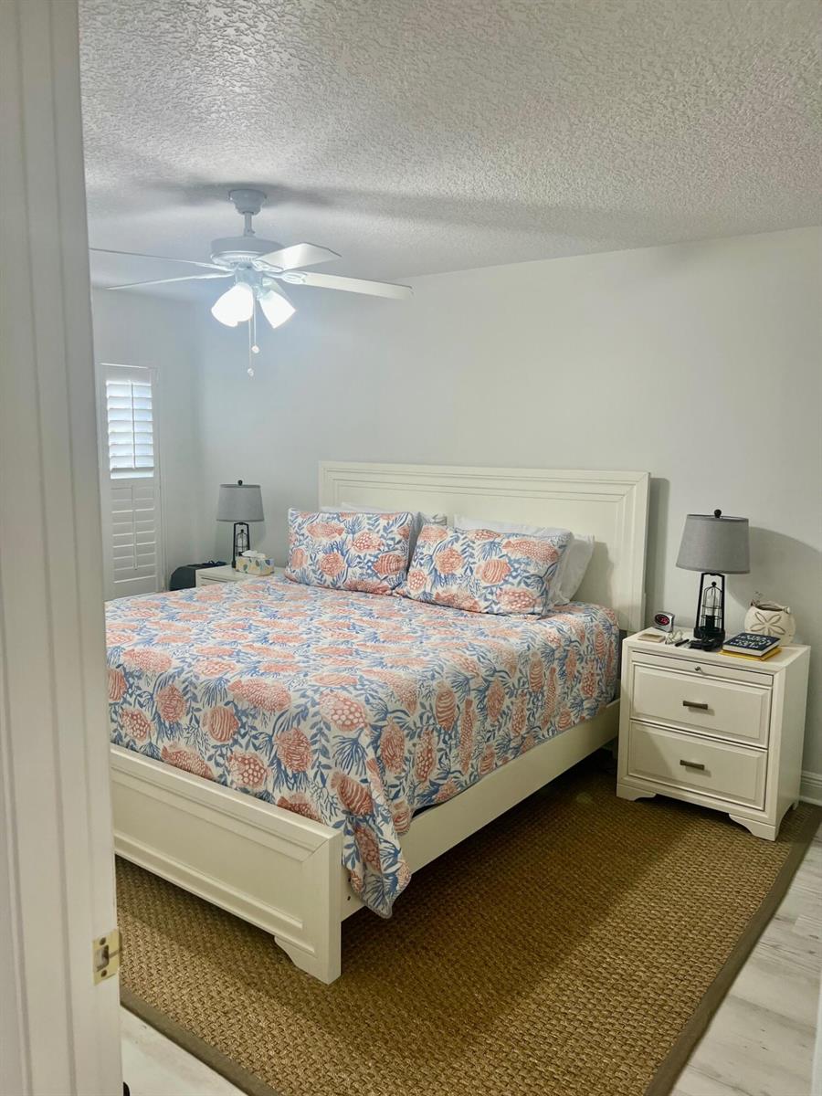 A bedroom features a white bed frame, patterned bedding, two nightstands, and a ceiling fan — 1209 Ocean Dunes Circle, Jupiter FL 33477, JUPITER, FL