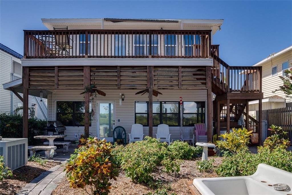 The exterior of a two-story house features a wooden deck, stairs, and a ground-level patio — 18521 GULF BOULEVARD, INDIAN SHORES, FL