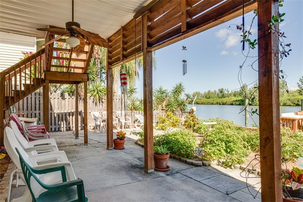 A covered concrete patio features a wooden staircase, outdoor furniture, and a view of water — 18521 GULF BOULEVARD, INDIAN SHORES, FL