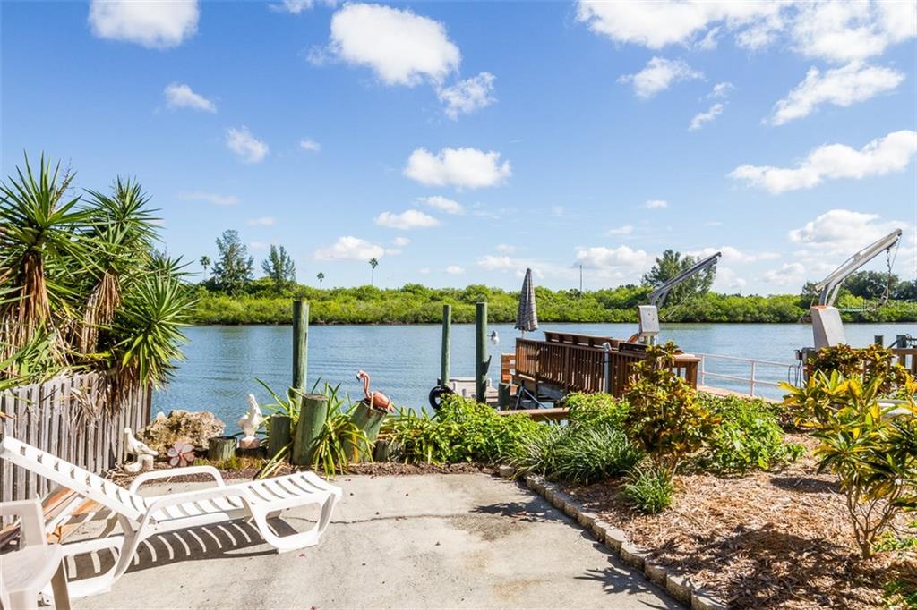 A concrete patio overlooks a canal with a wooden dock and boat lift — 18521 GULF BOULEVARD, INDIAN SHORES, FL