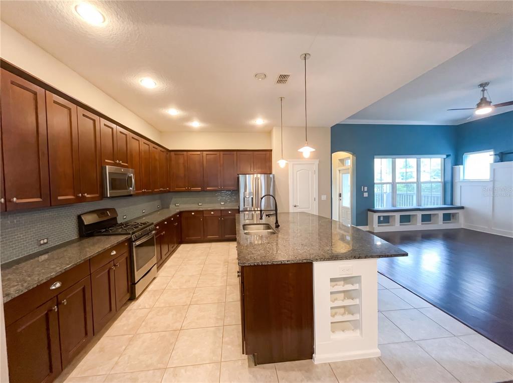 A kitchen with dark wood cabinets, granite countertops, and a large island overlooks a living area — 1338 UNION CLUB DRIVE, WINTER GARDEN, FL