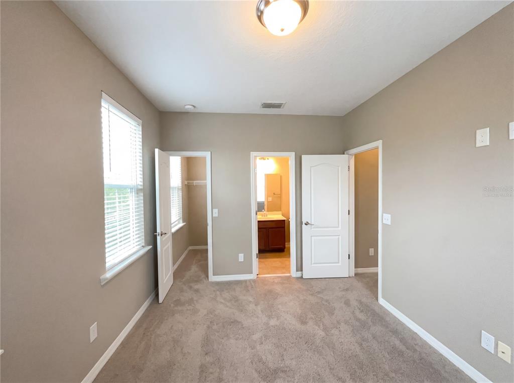 A bedroom with beige walls, carpeted flooring, a window, and doors leading to a closet and bathroom — 1338 UNION CLUB DRIVE, WINTER GARDEN, FL