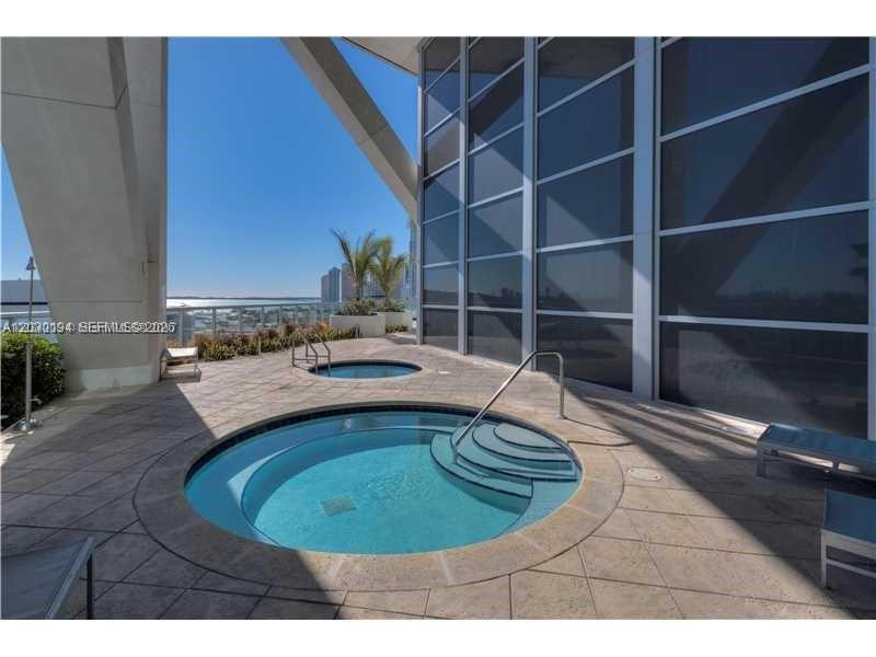 A circular hot tub sits on a tiled patio next to a modern glass building — 888 Biscayne Blvd # 2911, Miami FL 33132, MIAMI, FL