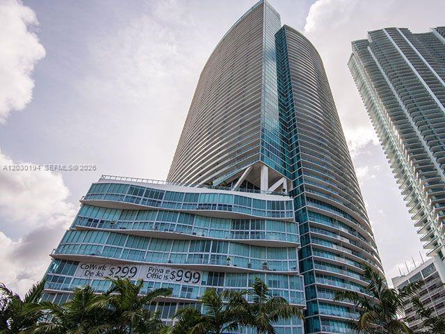 A low-angle view of a modern glass skyscraper with a curved facade and palm trees — 888 Biscayne Blvd # 2911, Miami FL 33132, MIAMI, FL