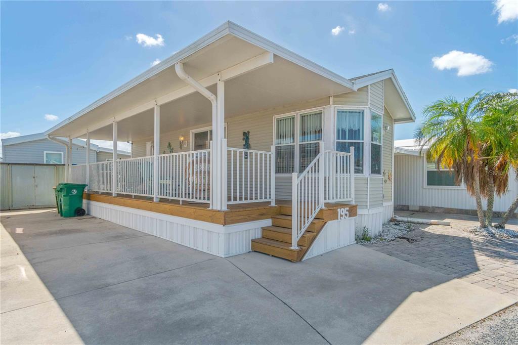 A manufactured home features a covered wooden porch with white railings and a concrete driveway — 1475 FLAMINGO DRIVE UNIT 195, ENGLEWOOD, FL