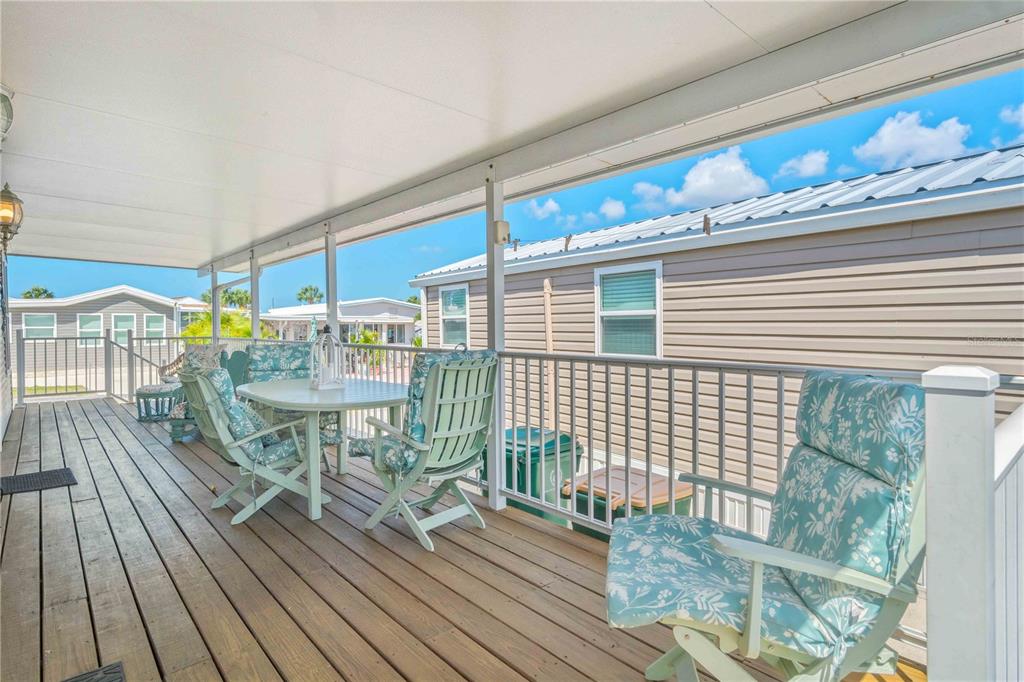 A covered wooden deck features a dining set with floral cushions and white metal railings — 1475 FLAMINGO DRIVE UNIT 195, ENGLEWOOD, FL