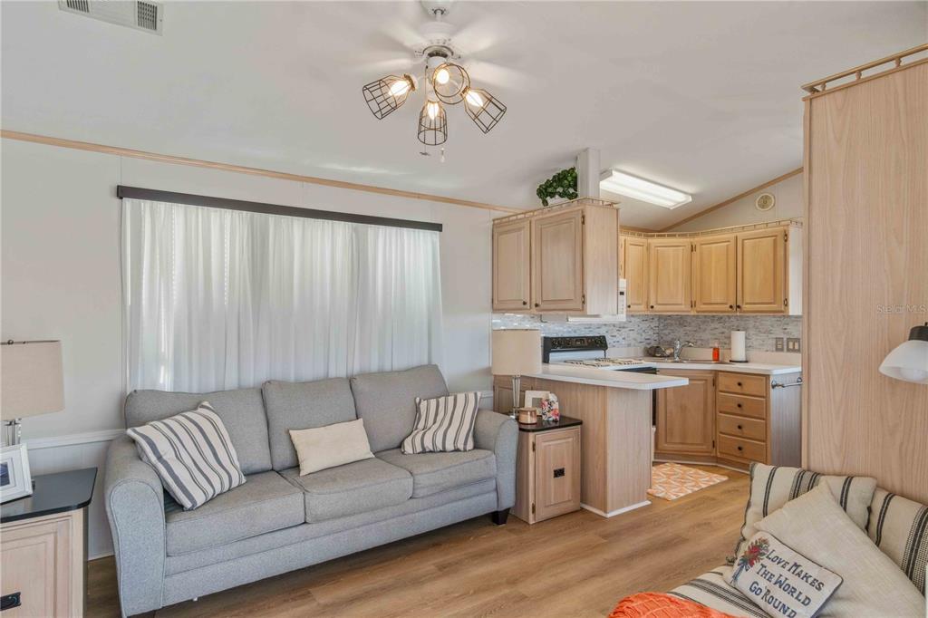 A living room with a grey sofa opens into a kitchen with light wood cabinets — 1475 FLAMINGO DRIVE UNIT 195, ENGLEWOOD, FL