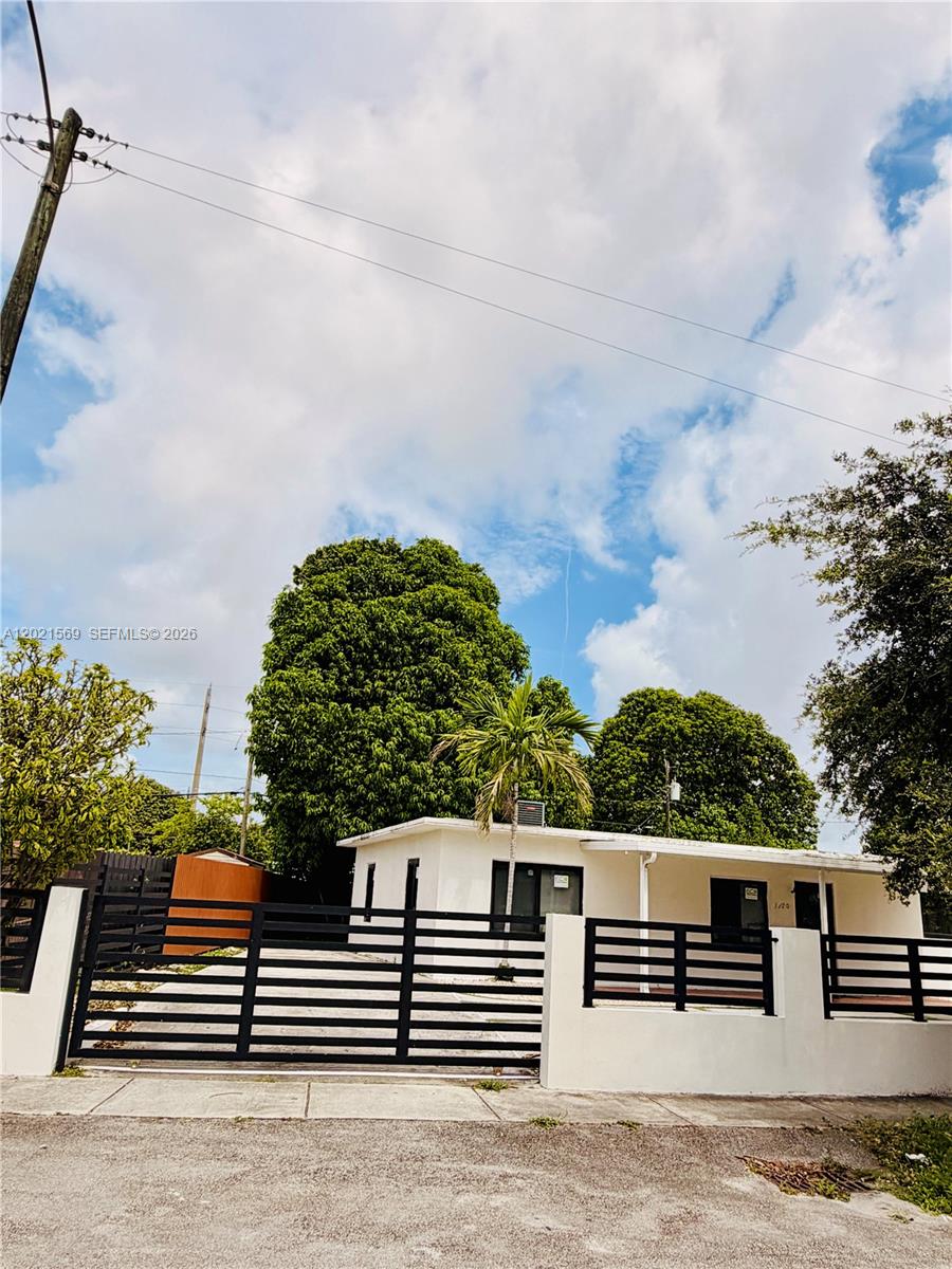 A white single-story house with a black metal fence and gate sits behind a sidewalk — 1120 E 6th Ct, Hialeah FL 33010, HIALEAH, FL