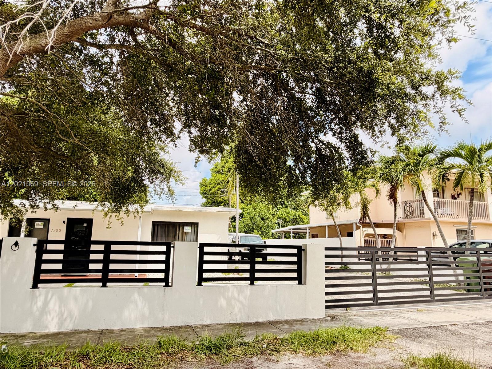 A white single-story house sits behind a modern black horizontal slat fence and gate — 1120 E 6th Ct, Hialeah FL 33010, HIALEAH, FL