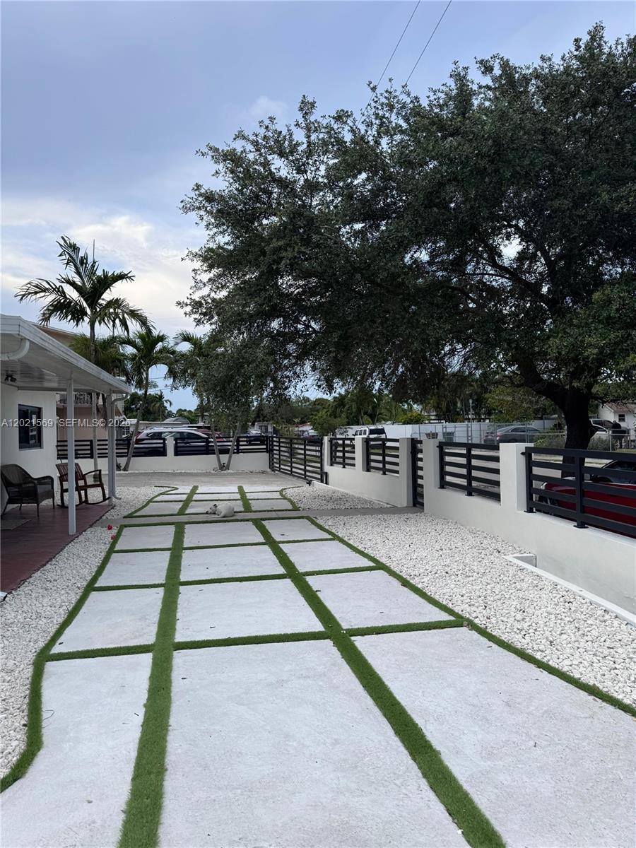 A paved driveway with grass strips leads to a fenced yard with a large tree — 1120 E 6th Ct, Hialeah FL 33010, HIALEAH, FL