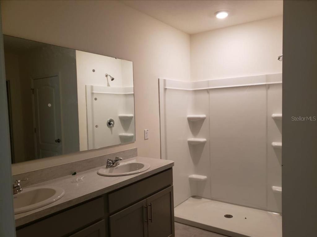 A bathroom features a double vanity with a mirror and a white walk-in shower — 713 FULMAR COURT, POINCIANA, FL