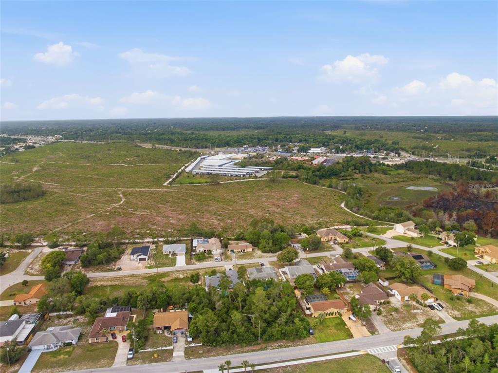 An aerial view shows a residential neighborhood bordering a large, undeveloped field and storage facility — 6011 FREEPORT DRIVE, SPRING HILL, FL