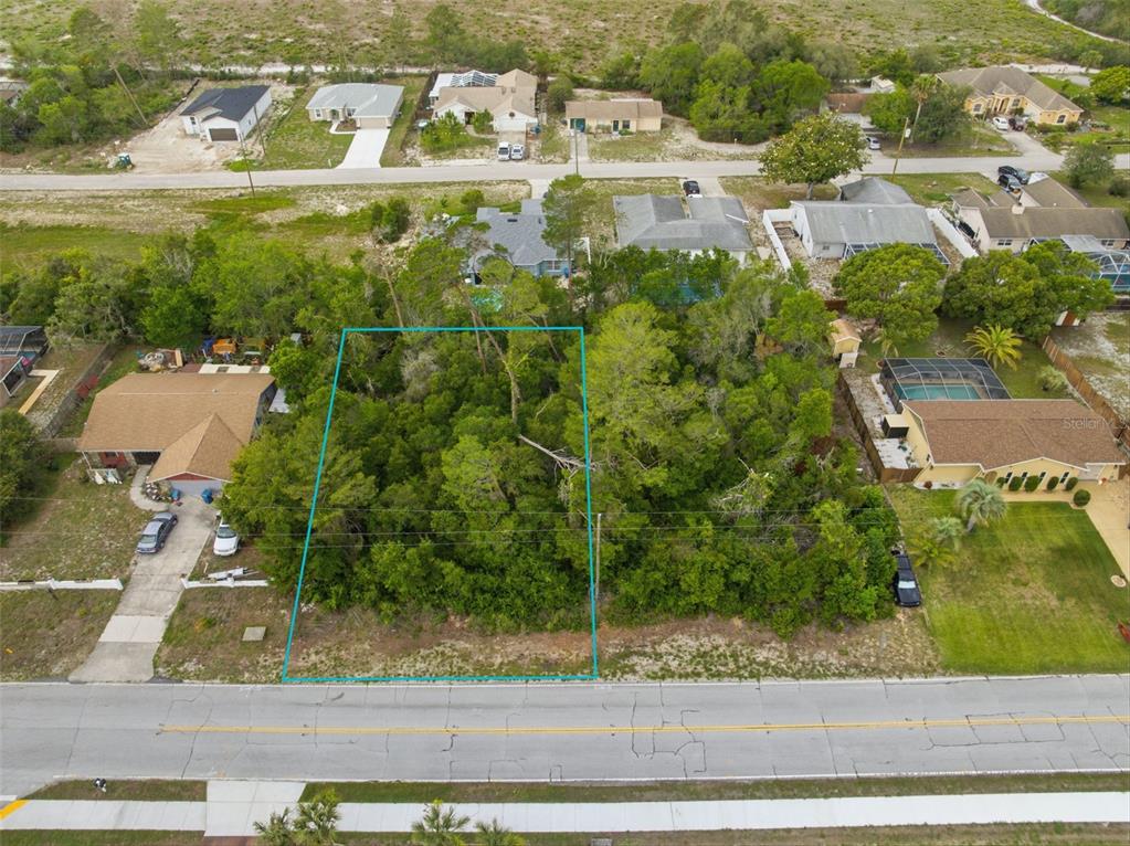 An aerial view shows a vacant, wooded lot outlined in blue between two residential houses — 6011 FREEPORT DRIVE, SPRING HILL, FL