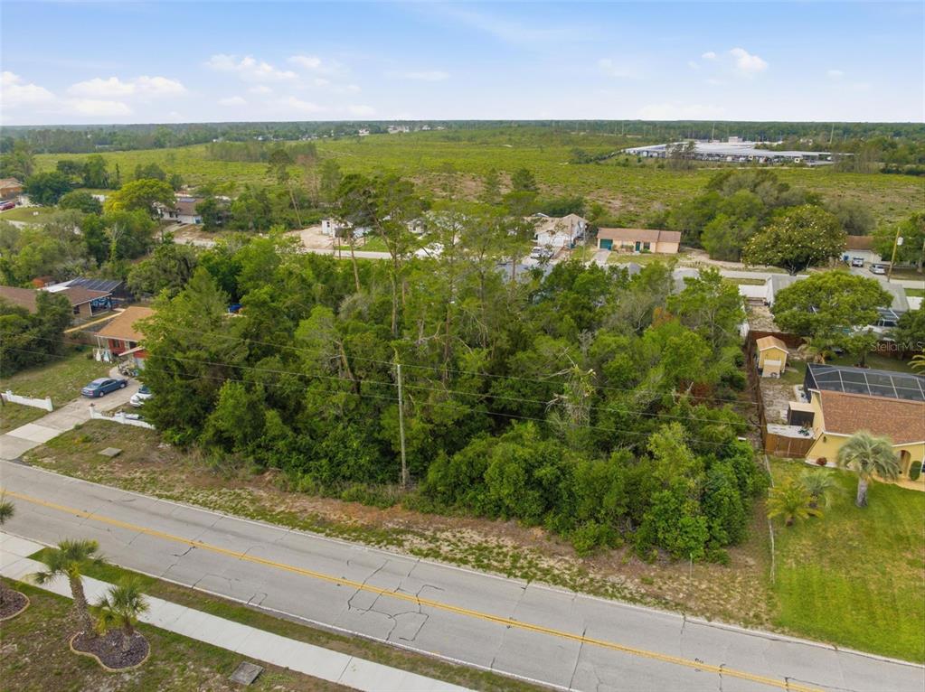 An aerial view shows a vacant, tree-covered lot situated between two residential houses — 6011 FREEPORT DRIVE, SPRING HILL, FL