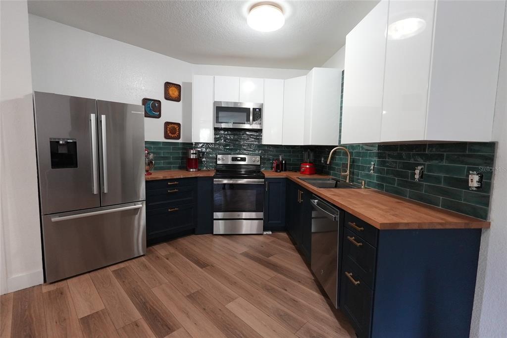 A kitchen features dark blue lower cabinets, white upper cabinets, wood countertops, and green tile — 911 N ORANGE AVENUE UNIT 248, ORLANDO, FL