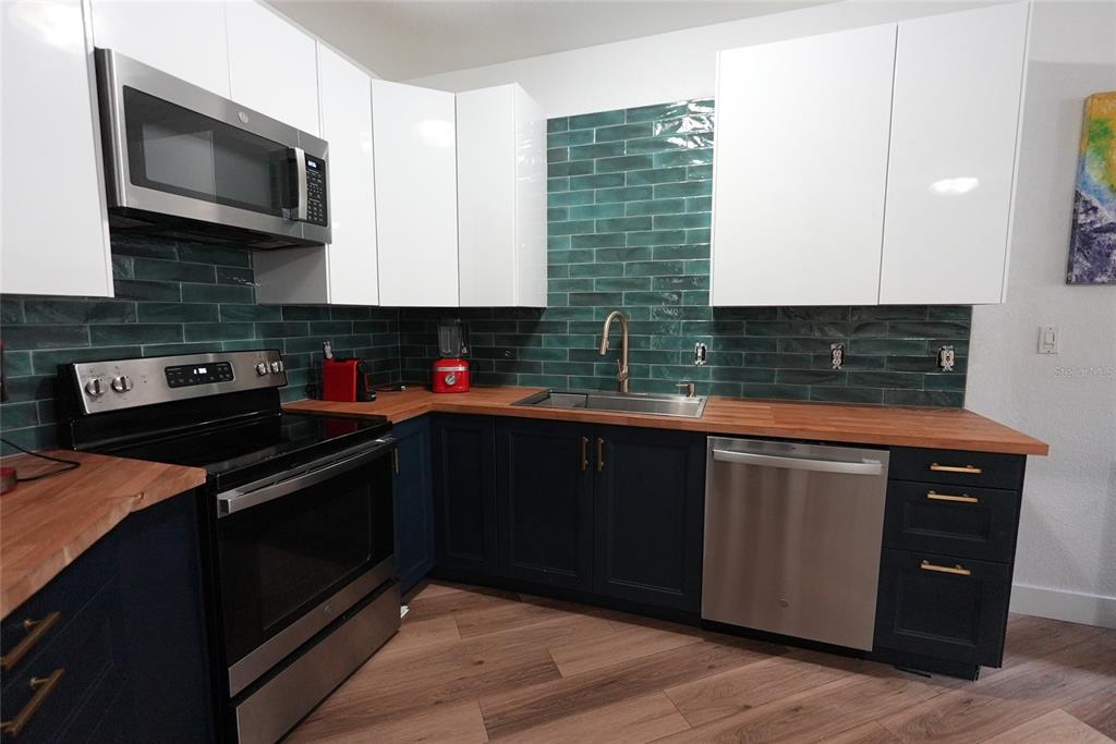 A kitchen features dark blue lower cabinets, white upper cabinets, wood countertops, and green tile — 911 N ORANGE AVENUE UNIT 248, ORLANDO, FL