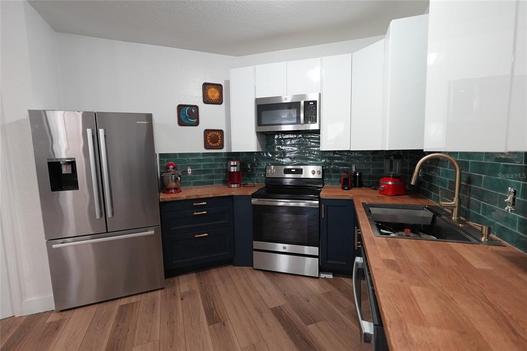 A kitchen features dark blue lower cabinets, white upper cabinets, wood countertops, and green tiles — 911 N ORANGE AVENUE UNIT 248, ORLANDO, FL
