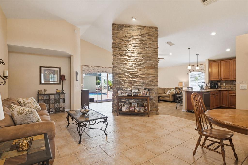 A living room and kitchen area feature a central stone fireplace and tile flooring — 3228 BENTLEY DRIVE, PALM HARBOR, FL