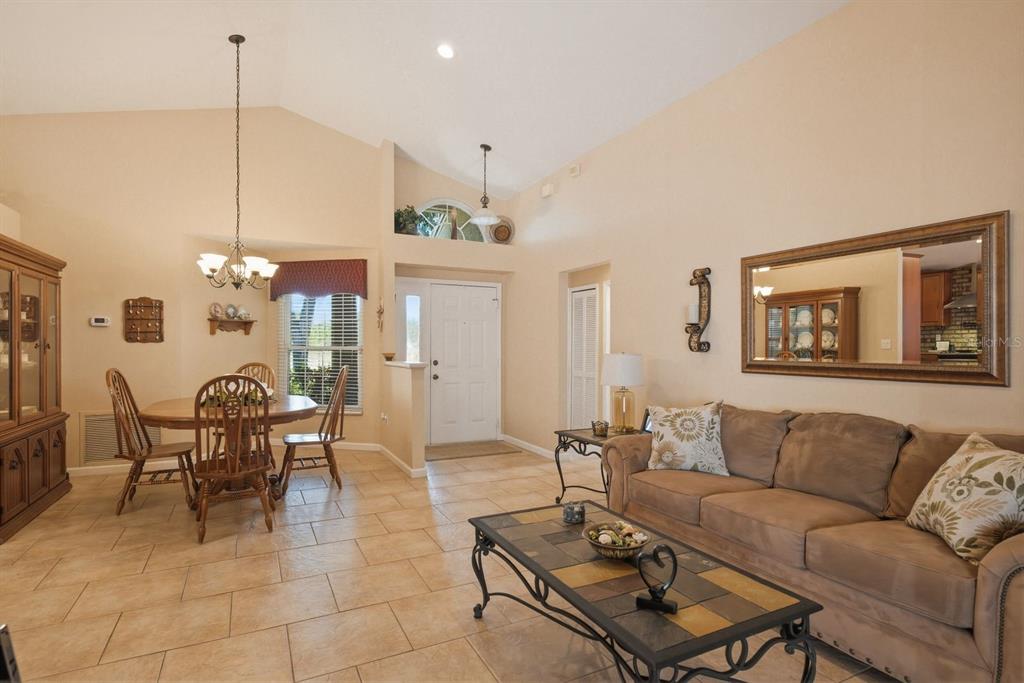 A living and dining room with tile floors, vaulted ceilings, and a brown sofa — 3228 BENTLEY DRIVE, PALM HARBOR, FL