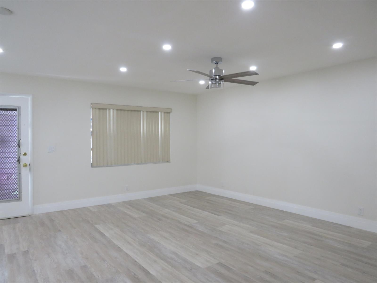 A bright, empty room features light wood-look flooring, white walls, recessed lighting, and a ceiling fan — 557 Burgundy L, Delray Beach FL 33484, DELRAY BEACH, FL