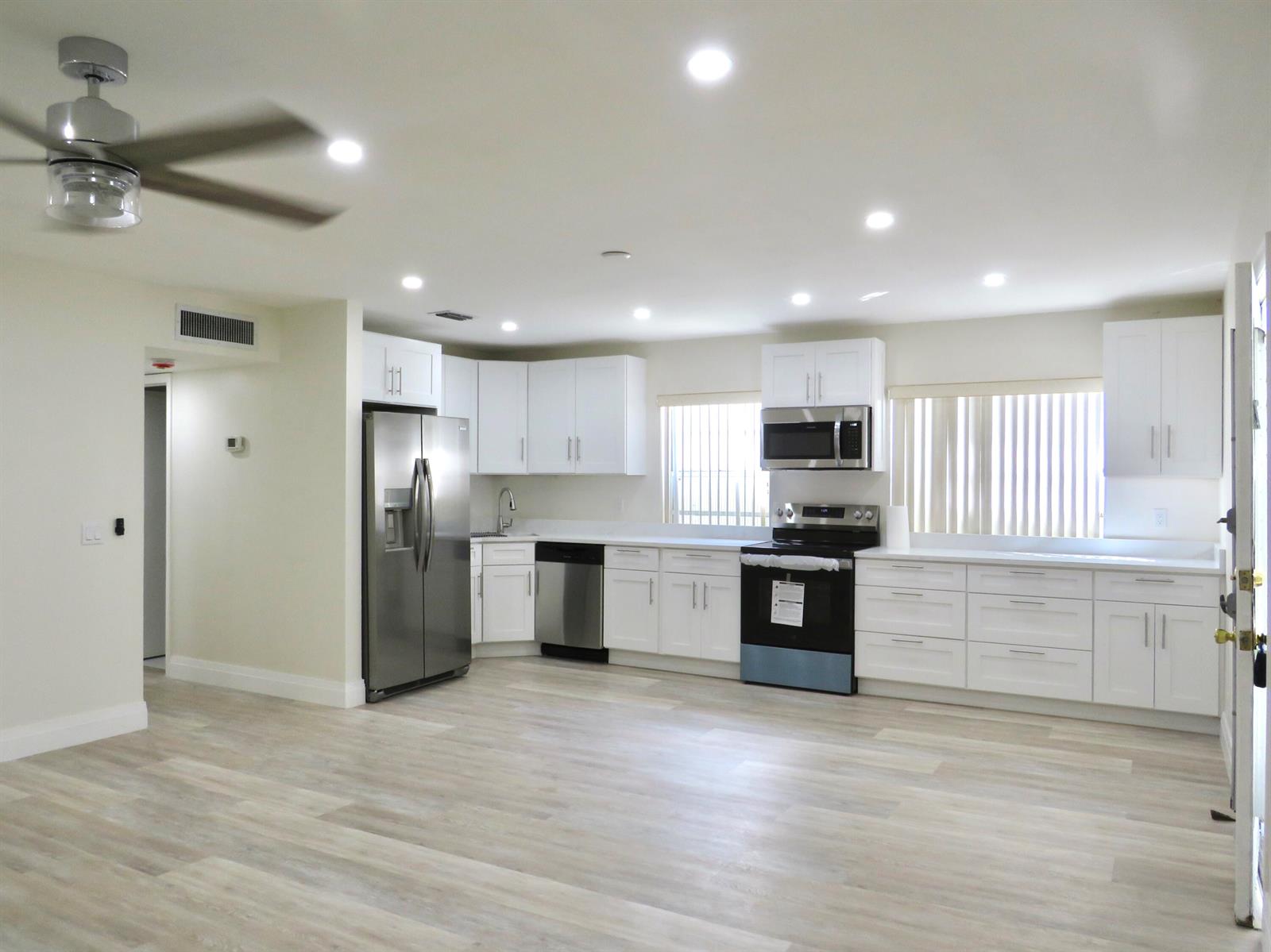 A modern kitchen features white cabinets, stainless steel appliances, and light wood-look flooring — 557 Burgundy L, Delray Beach FL 33484, DELRAY BEACH, FL