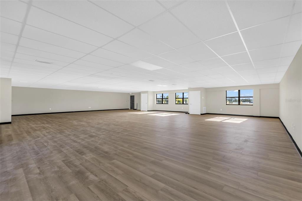 A large, empty room with light wood-look flooring, white walls, and a drop ceiling — 3596 TAMIAMI TRAIL, PORT CHARLOTTE, FL